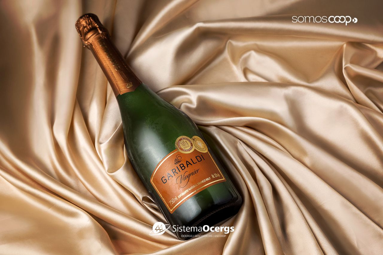 Garrafa de espumante Garibaldi Viognier deitada sobre tecido acetinado dourado, com rótulo em destaque e medalhas de premiação visíveis.