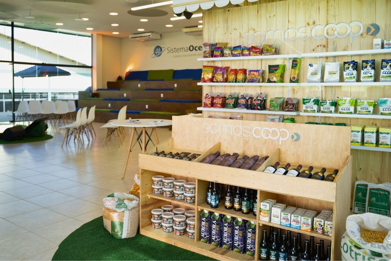Espaço do Sistema Ocergs na Expodireto Cotrijal, destacando produtos de cooperativas gaúchas. O estande exibe alimentos, bebidas e itens agroindustriais com a identidade &quot;Somos Coop&quot;.